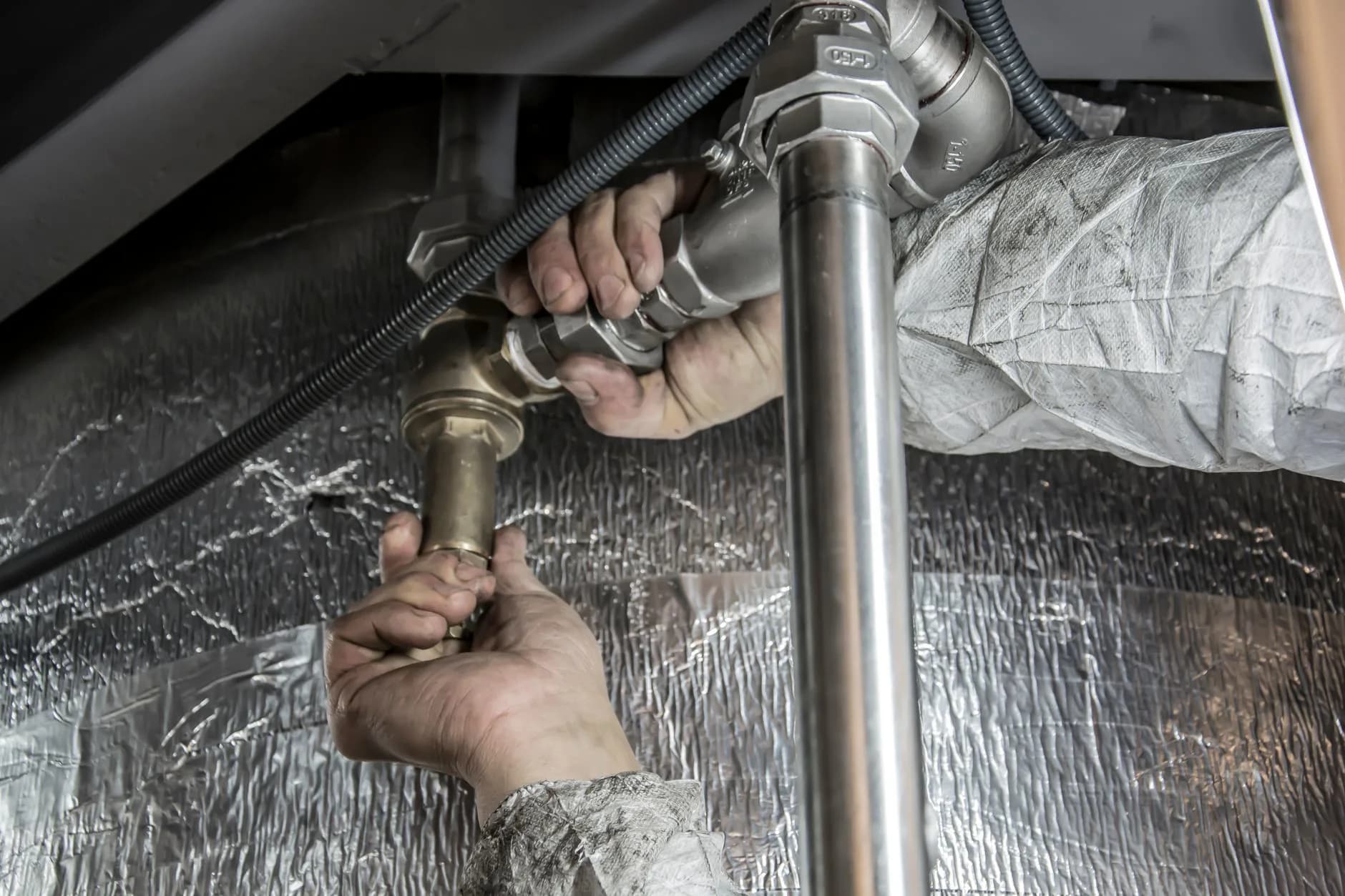 A plumber working on supply lines under a kitchen sink