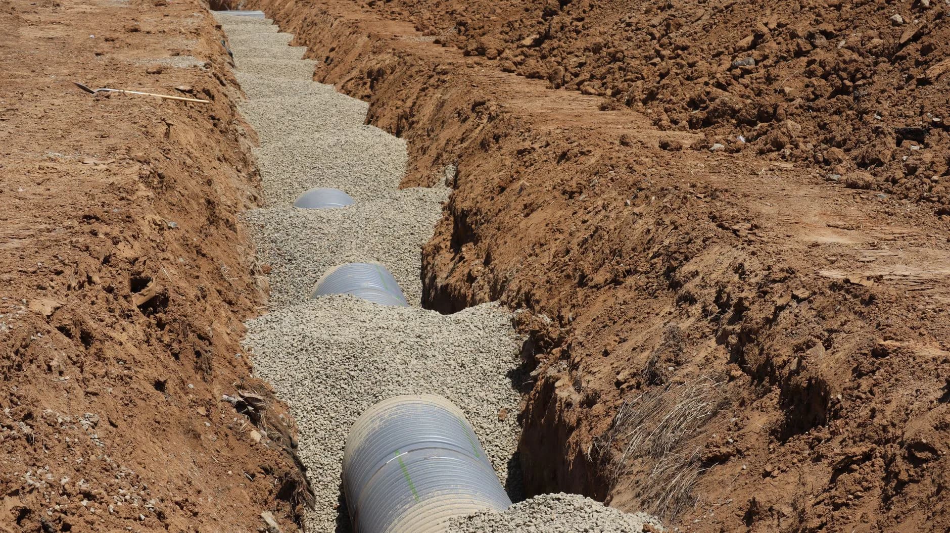An open trench exposing a sewer line running from a house toward the street