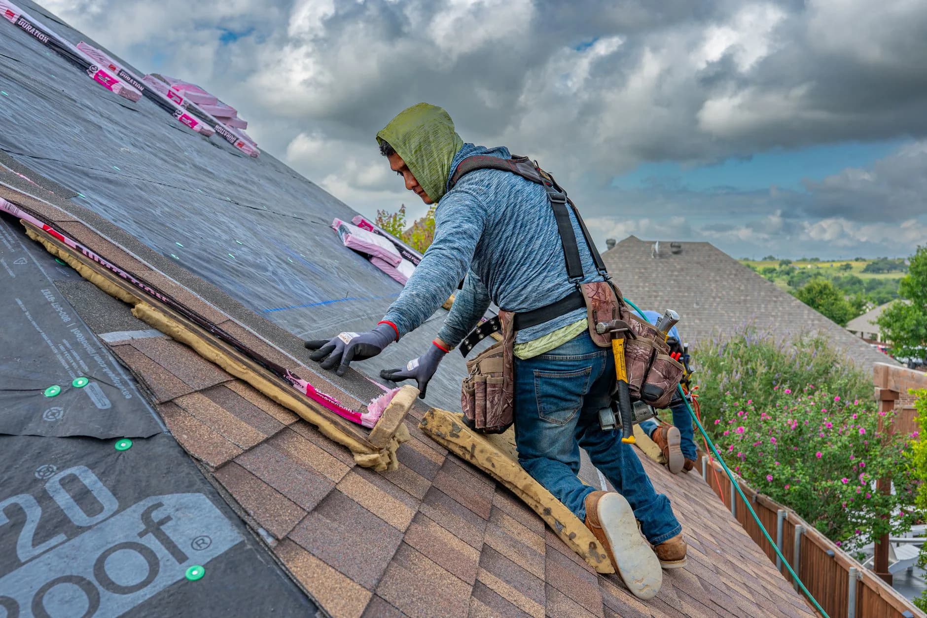 Roofers nailing down a course of asphalt shingles on a residential roof