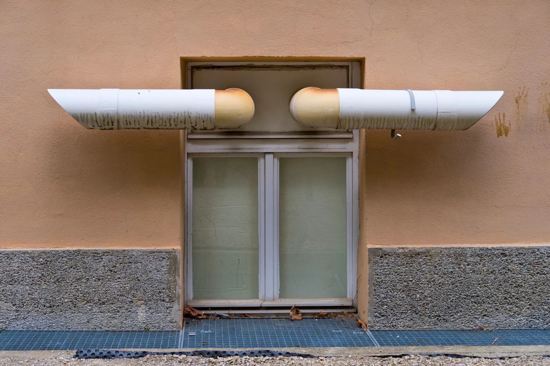 Two white plastic pipes exiting the side wall of a house