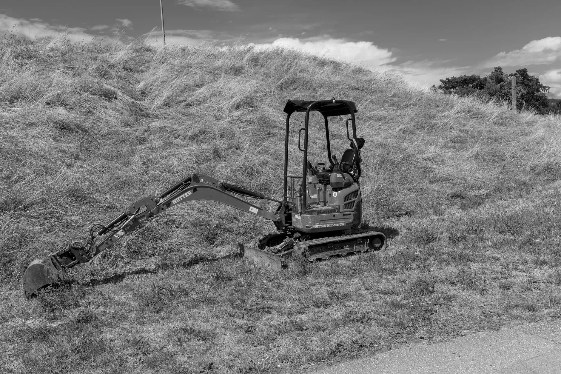 A small tracked excavator lifting a boulder into place in a yard