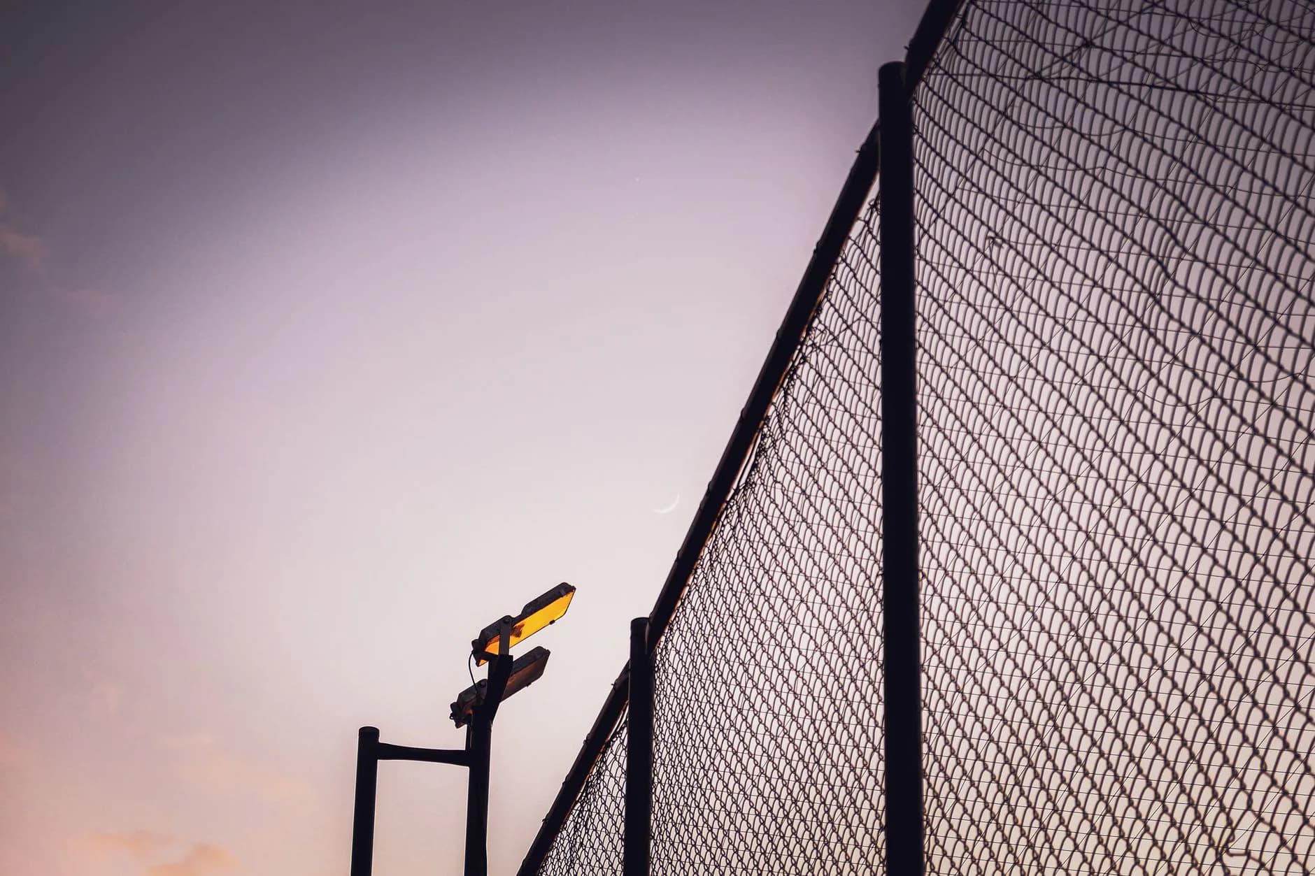 A chain link fence corner post with tension bands holding the stretched fabric