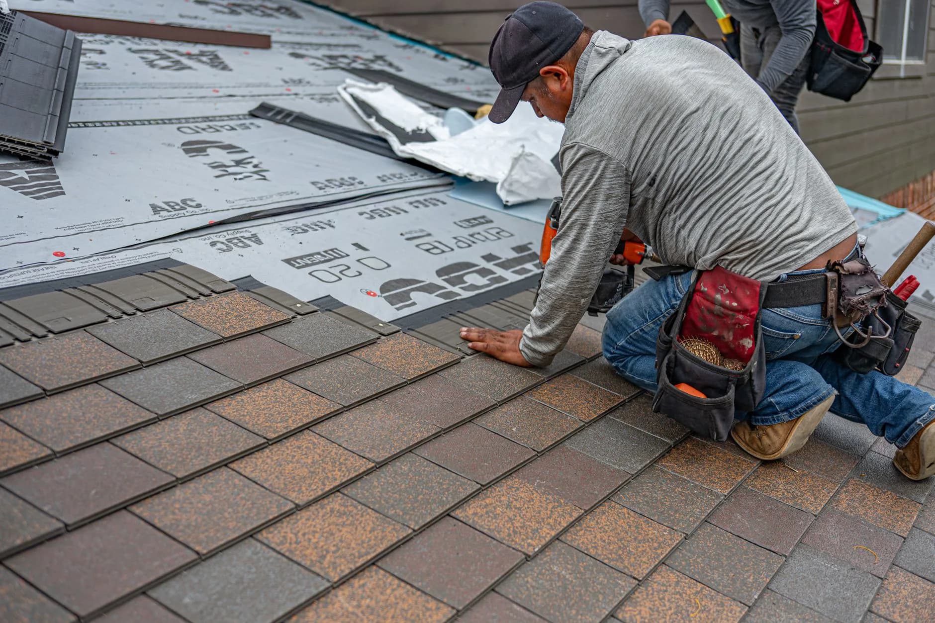 A roofer nailing new asphalt shingles onto a roof